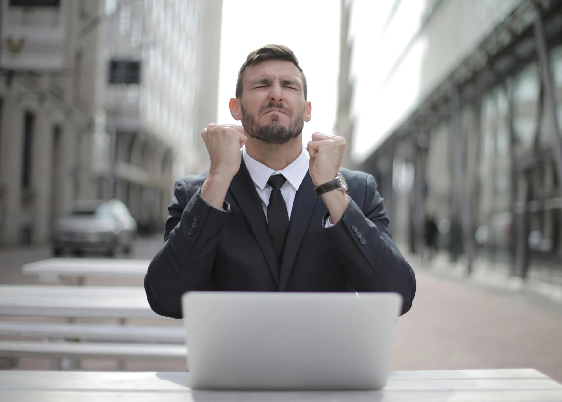 Frustrated businessman clenching fists in front of laptop outdoors.