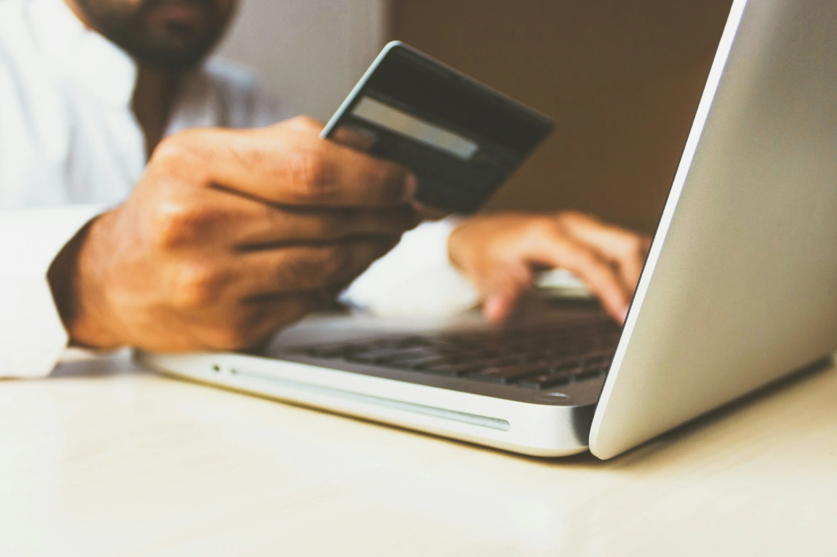 Hand holding a card in front of a laptop.