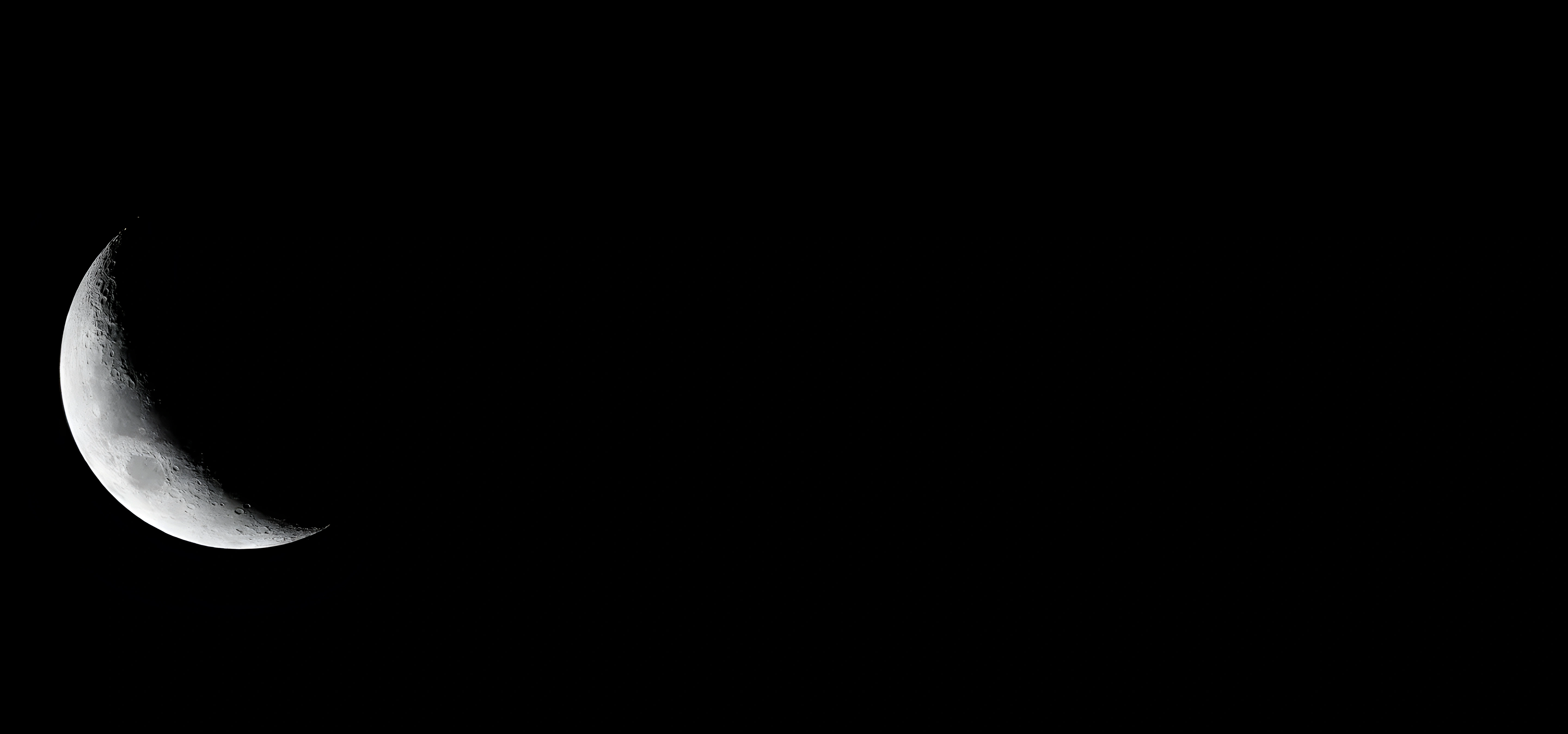A crescent moon with visible craters set against a black background.