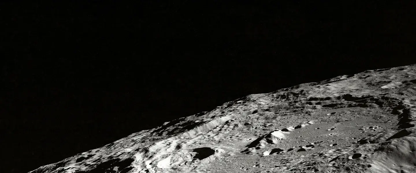 A black and white view of a cratered lunar surface sloping upward against the black void of space.